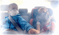 Two young children sitting in the back seat of a car wearing masks to protect them from smoke.